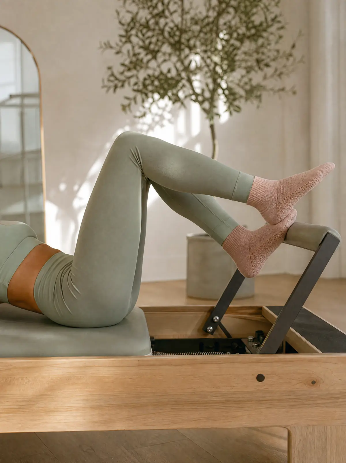 Feet in blush closed-toe grip socks pressing a reformer foot bar